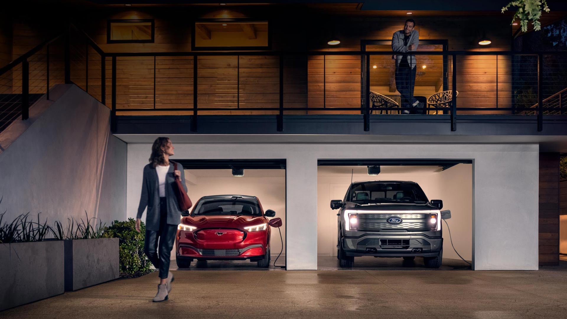 Woman walking out from home garage with a 2024 Mustang® Mach-E and Ford Lightning® truck in plugged-in and charging | Apple Ford Shakopee in Shakopee MN